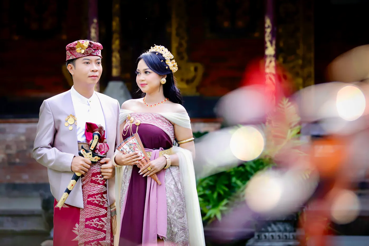 Pasangan mengenakan busana adat Bali di halaman rumah tradisional